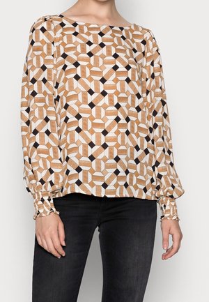 Blouse à manches longues avec un motif géométrique en noir, blanc et beige. Présente des poignets froncés et un col large. Tissu doux.