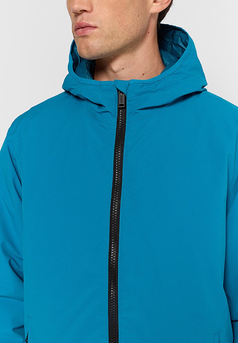 Giacca turchese con zip frontale, cappuccio e texture liscia. Presenta una zip nera e un design minimale. Nessun logo o motivo visibile.