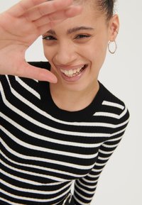 Pull à côtes rayé noir et blanc avec un col rond. Modèle faisant un geste ludique, avec des boucles d'oreilles créoles.