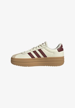 Zapatilla blanca de cuero con rayas burdeos, suela de goma, punta redonda y acentos texturizados. Presenta cordones y un logo de la marca en el talón.
