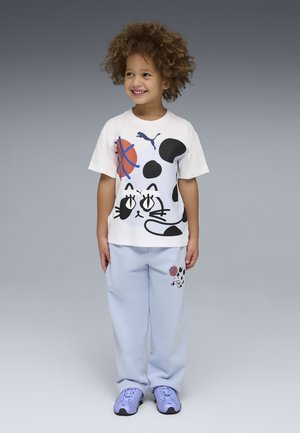 Smiling child wearing white T-shirt and light blue pants with black and white cartoon cat and basketball designs, standing against gray background.