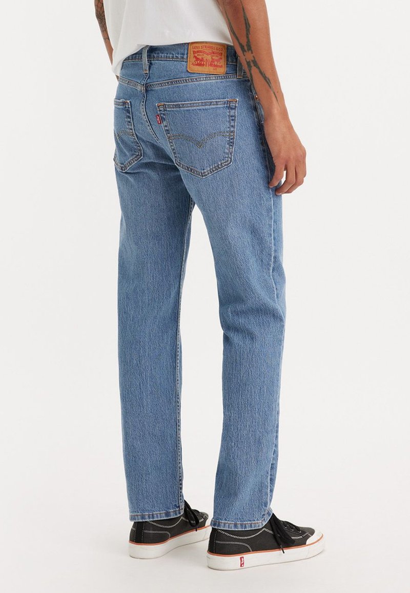 Vaqueros de denim azul claro con un corte relajado, que presentan un parche de logo rojo en la cinturilla trasera y dos bolsillos traseros. Llevados con zapatillas negras.