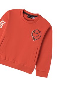 Felpa rossa con scollatura rotonda, polsini e orlo a coste. Presenta una toppa con un viso sorridente e la parola "DAY" stampata sul maniche sinistro.