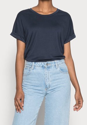 T-shirt bleu marine à manches courtes avec des ourlets retroussés, composé d'un matériau doux. Associé à un jean en denim léger taille haute avec une coupe décontractée.