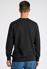 Musta svetari pitkillä hihoilla ja pyöreällä pääntiellä, jossa on resorit helmassa ja hihansuut, yhdistetty sinisiin farkkuihin. Tasainen kangaspinta.