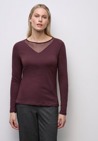 Maglia a maniche lunghe color bordeaux con scollatura a V in rete trasparente. Vestibilità slim e texture liscia, abbinata a pantaloni grigi.