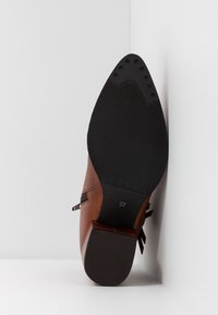 Botte cheville en cuir marron avec une semelle en caoutchouc noir, fermeture éclair sur le côté, et taille 37 indiquée sur la semelle.
