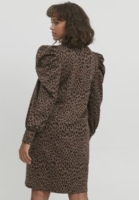 Robe à imprimé léopard dans des tons de marron, présentant des manches ballon, une silhouette ajustée et un ourlet au genou. Tissu texturé avec une finition douce.