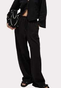 Czarne, szerokie spodnie z fakturowanej tkaniny z elastycznym pasem na sznurki, zestawione z krótkim czarnym topem i wzorzastą torbą.