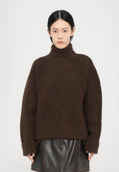 Pull en maille brun avec un col roulé côtelé haut. Présente des manches oversize et une finition texturée. Les bords sont également côtelés.