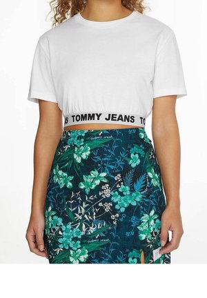 Wit cropped T-shirt met een zwarte "Tommy Jeans" tailleband, gecombineerd met een marineblauwe rok met bloemenpatroon met groene en witte bloemen.