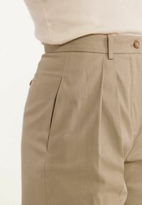 Pantalons plissés beiges en tissu texturé, dotés d'une fermeture à boutons et de poches latérales pour plus de fonctionnalité.
