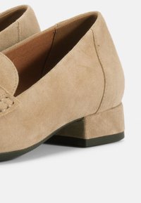 Μπεζ σουέντ μοκασίνια με χαμηλό τακούνι, με στρογγυλεμένη μύτη και διακριτική ραφή στο μπροστινό μέρος. Μαλακή υφή με μικρό τακούνι τύπου block.