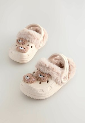 Zoccoli beige chiaro con una morbida fascia in pelliccia rosa, dotati di due dettagli a forma di faccia d'orso e fori di ventilazione. Suola texturizzata per una migliore aderenza.