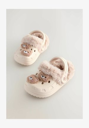 Zoccoli beige chiaro con una morbida fascia in pelliccia rosa, dotati di due dettagli a forma di faccia d'orso e fori di ventilazione. Suola texturizzata per una migliore aderenza.