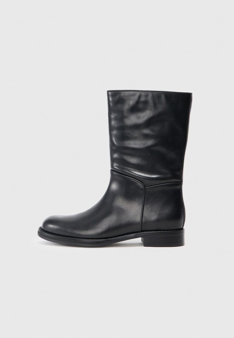 Bottines en cuir noir avec une texture lisse, bout rond et petit talon carré. Le design présente une tige légèrement relâchée.