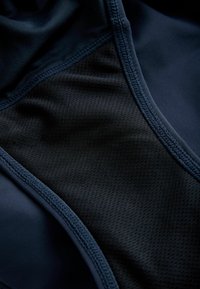 Artimas mėlynos tamsios medžiagos vaizdas su juodos tekstūrinės tinklinės dalies ir detaliu siuvimo siūlių apdirbimu.