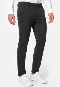 Mørkegrå slim-fit bukser laget av et mykt stoff med en glatt tekstur, med knappelukking og sidelommer, kombinert med hvite sneakers.
