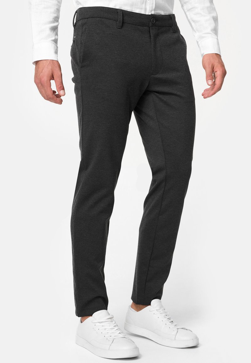 Mørkegrå slim-fit bukser laget av et mykt stoff med en glatt tekstur, med knappelukking og sidelommer, kombinert med hvite sneakers.