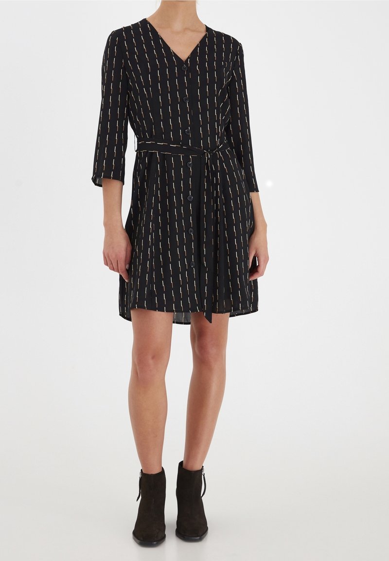 Robe noire avec col en V, manches trois-quarts et ceinture. Présente des lignes verticales jaunes et blanches ainsi que des détails de boutons sur le devant.