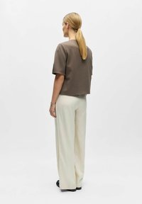 Haut court marron à manches courtes associé à un pantalon large crème, vu de dos sur un fond uni.