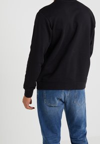 Svart sweatshirt med långa ärmar, rund halsringning och ribbade muddar, kombinerad med blekta blå denimjeans. Inga synliga mönster eller detaljer.