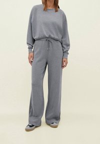 Set da lounge grigio composto da una felpa comoda e pantaloni larghi con vita regolabile, realizzati in tessuto morbido. Accentuato con scarpe casual.