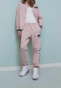 Ljusrosa Nike sweatshirt med svarta detaljer, matchad med joggers som har svarta sidosträck och logotyp, bärs med vita sportskor.