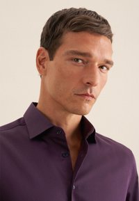 Camicia button-up viola con colletto strutturato, texture liscia e bottoni scuri. Ingrandimento dei dettagli del tessuto e del colletto.