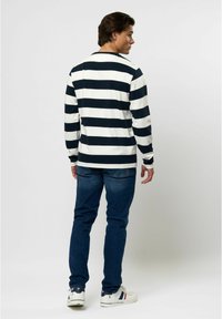 Langarm polo shirt met marineblauwe en witte horizontale strepen. Gemaakt van zachte stof, heeft een ronde hals en geribde manchetten. G gedragen met blauwe jeans.