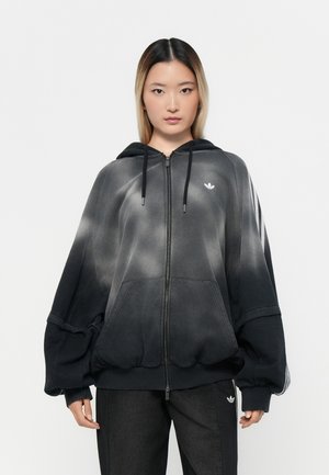 Hoodie à zip noir dégradé avec capuche, design oversize et poche kangourou. Présente un logo blanc sur la poitrine et des poignets côtelés.
