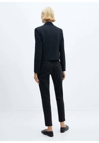 Blazer negro corto con un diseño limpio, combinado con pantalones de mezclilla negros ajustados. Textura suave y detalles mínimos de hardware.