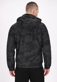 Jachetă neagră cu un model, având glugă și un design geometric texturat. Manșete și tiv elastic, fabricată dintr-un material ușor.