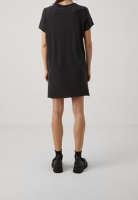 Robe noire à manches courtes avec une coupe décontractée, une texture lisse et une longueur jusqu'au genou. Portée avec des chaussures noires cloutées et des chaussettes transparentes.