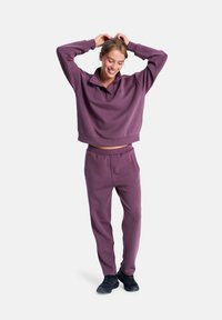 Ciemnofioletowy dres składający się z krótkiego, oversize'owego swetra z kołnierzykiem oraz dopasowanych spodni zwężających się ku dołowi. Materiał wydaje się miękki z minimalną teksturą.