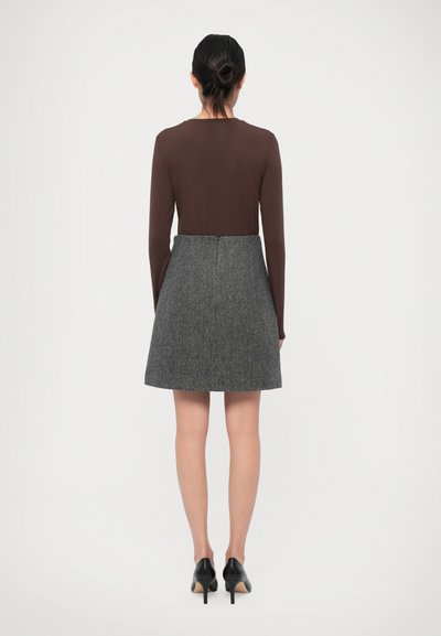 Bruine lange mouwtop gecombineerd met een grijze gemusterde rok. Zwarte hoge hakken maken de outfit compleet. Eenvoudig ontwerp en klassieke snit.