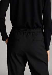 Schwarze Hose mit elastischem Bund, die zwei Gesäßtaschen und eine glatte Textur aufweist und für einen angenehmen Sitz gefertigt ist.