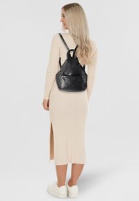 Schwarzer Leder-Rucksack in dreieckiger Form, mit einem oberen Tragegriff, verstellbaren Schulterriemen und einer Vordertasche. Glatte Oberfläche, minimale Hardware.