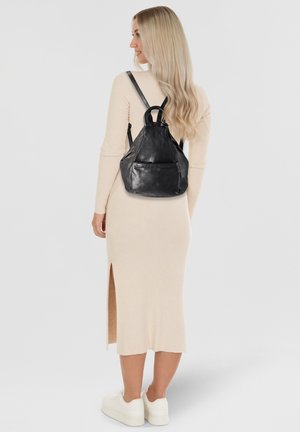 Black leather backpack with a triangular shape, featuring a top handle, adjustable straps, and a front pocket. Smooth texture, minimal hardware.