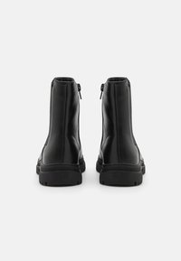Bottines noires en cuir avec une texture lisse, dotées d'une fermeture zippée à l'arrière et d'une semelle en caoutchouc robuste.
