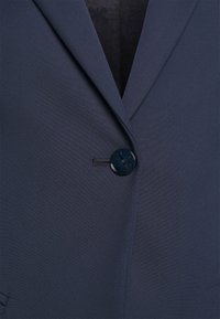 Tmavě námořnický blazer s texturovanou tkaninou, špicatými klopami a jedním kulatým zapínáním. Hladký povrch, přiléhavý střih.