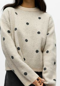 Cream-colored sweater with black polka dots, round neckline, ribbed cuffs, and hem. Soft texture with a relaxed fit.