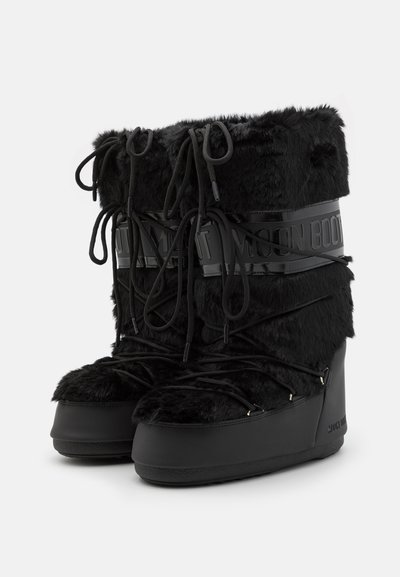 Bottes doublées de fourrure noire avec une semelle en caoutchouc noir brillant et un devant à lacets. Dotées d'un bandeau logo proéminent et d'un talon compensé pour plus de hauteur.