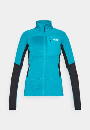 Ženska zip-up jakna v turkizni barvi z črnimi rokavi. Ima teksturiran vzorec, dva stranska žepa in majhen žepek na prsih.