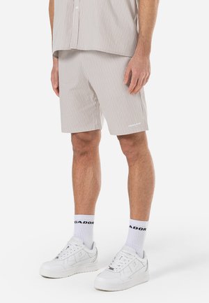 Shorts beige rayés avec une taille élastique, associés à des baskets blanches et des chaussettes mi-mollet. Le tissu est léger et lisse, offrant un look décontracté.