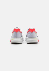 Vue arrière de chaussures de sport présentant un dessus en maille grise, des accents blancs et des détails en rouge vif et vert néon sur le talon et la semelle.