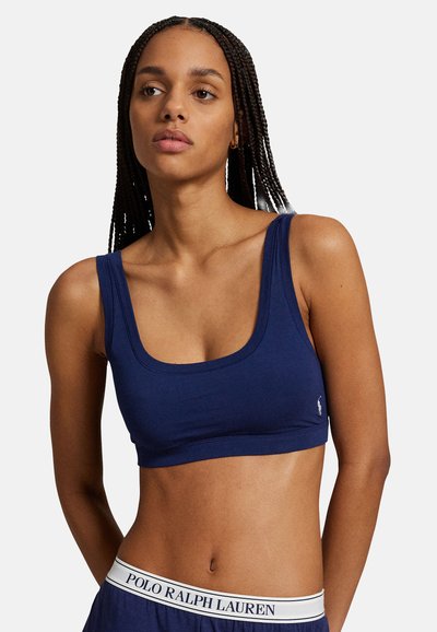 Tmavě modrý bavlněný bralet s širokými ramínky a zaobleným výstřihem. Na levé straně je malý logo, doplněný kalhotami s páskem s logem.