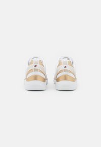 Baskets blanches avec des accents dorés et un dos texturé. Caractérisées par un matériau lisse, des motifs contrastés et une boucle de marque au talon.