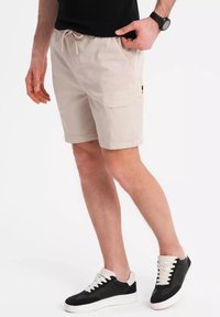 Shorts cargo beiges avec une taille élastique, poches latérales et une poche au dos, associés à des baskets noir et blanc.