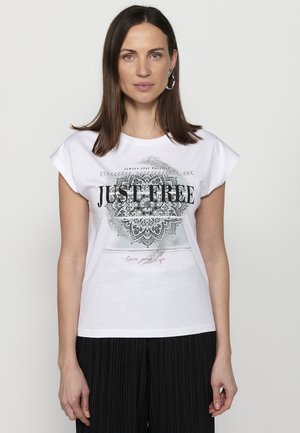 T-shirt en coton blanc à manches courtes avec un design graphique noir, texte "JUST FREE", et motif mandala décoratif. Pantalons plissés noirs.